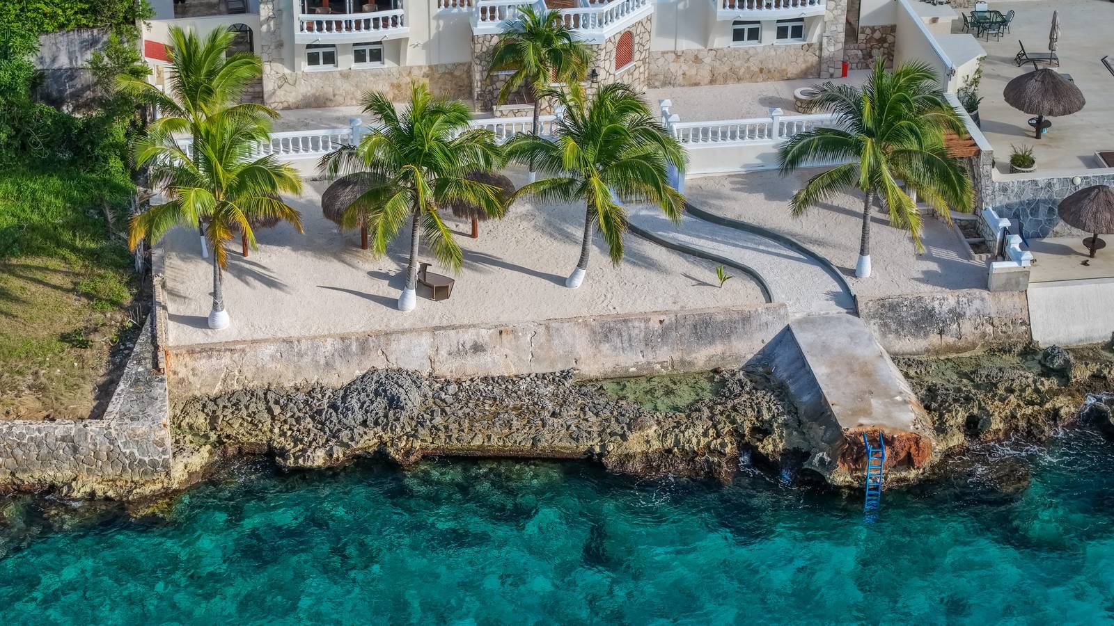 A sand terrace and palapas above the ironshore at an Island Casa home