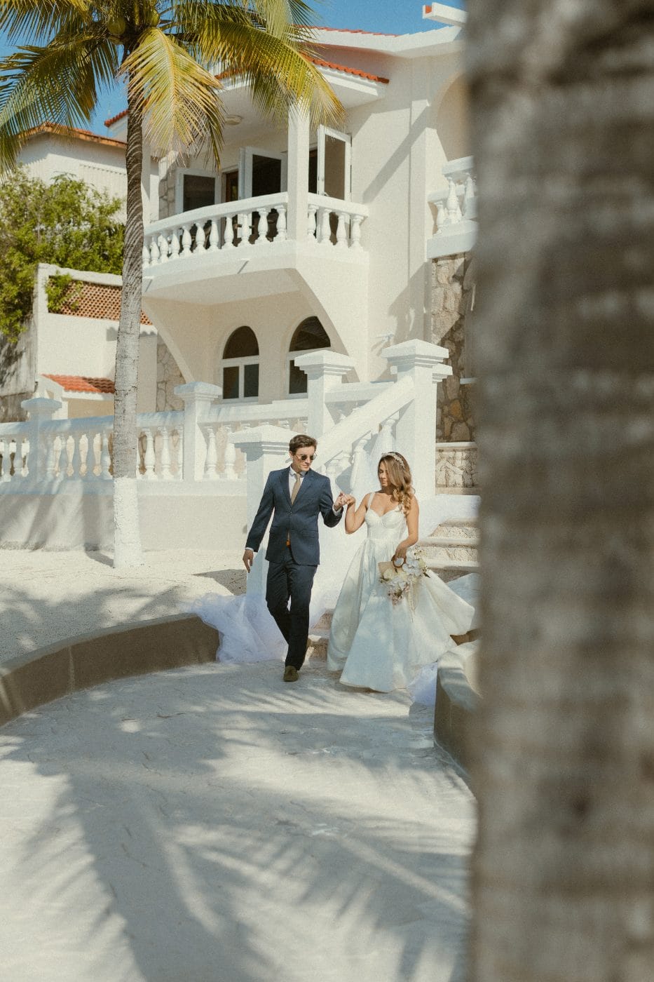 A couple coming down the stone stairs of the house, train trailing behind