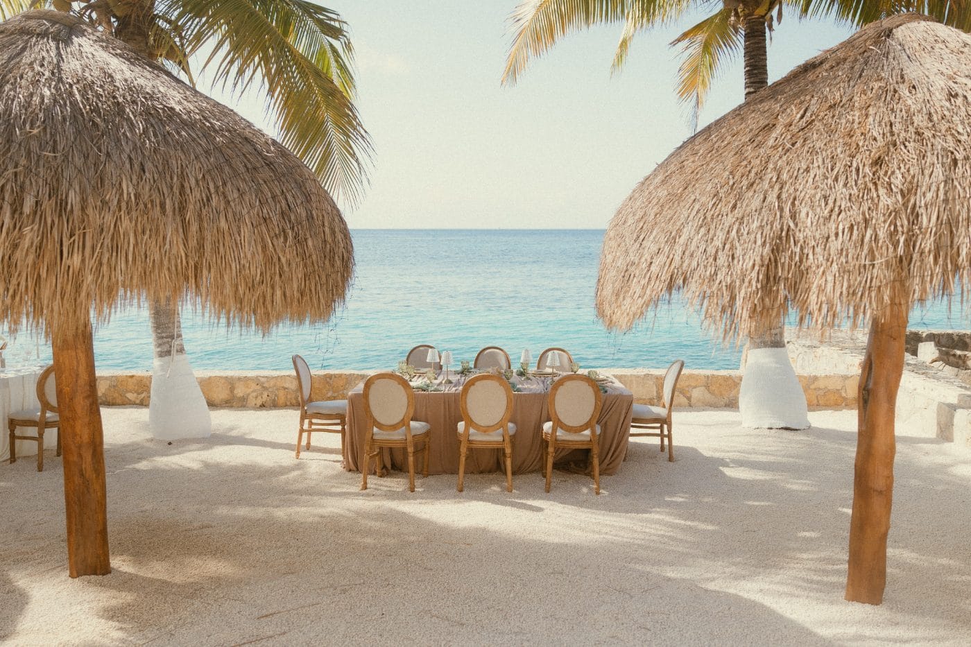 A round table in white linen and candles at dusk, the sea behind